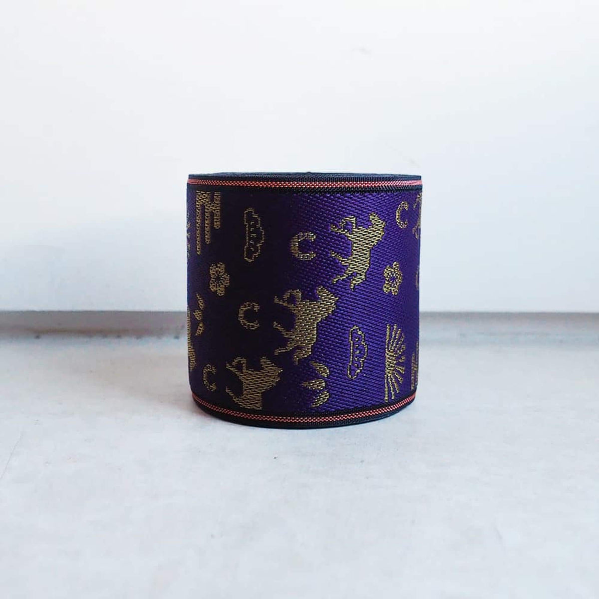 A purple and gold patterned bracelet or cuff is displayed on a white surface.