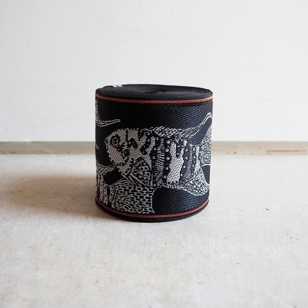 A black and white woven object with a fish design on it, sitting on a white surface.