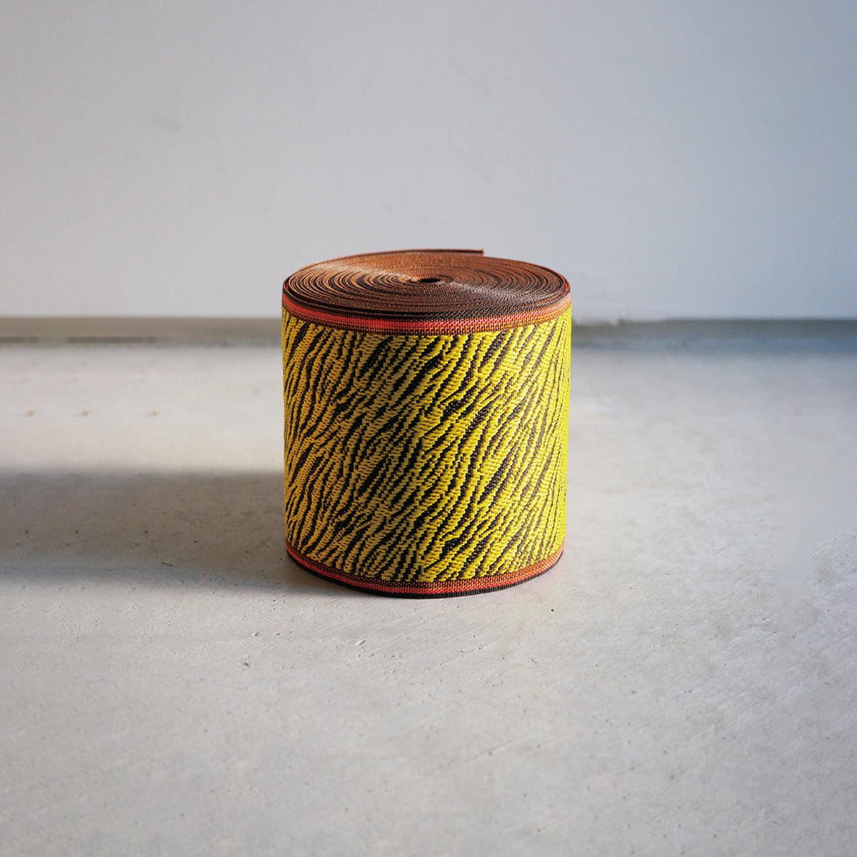 A cylindrical object with a zebra print pattern in yellow and black colors, sitting on a white surface against a plain background.