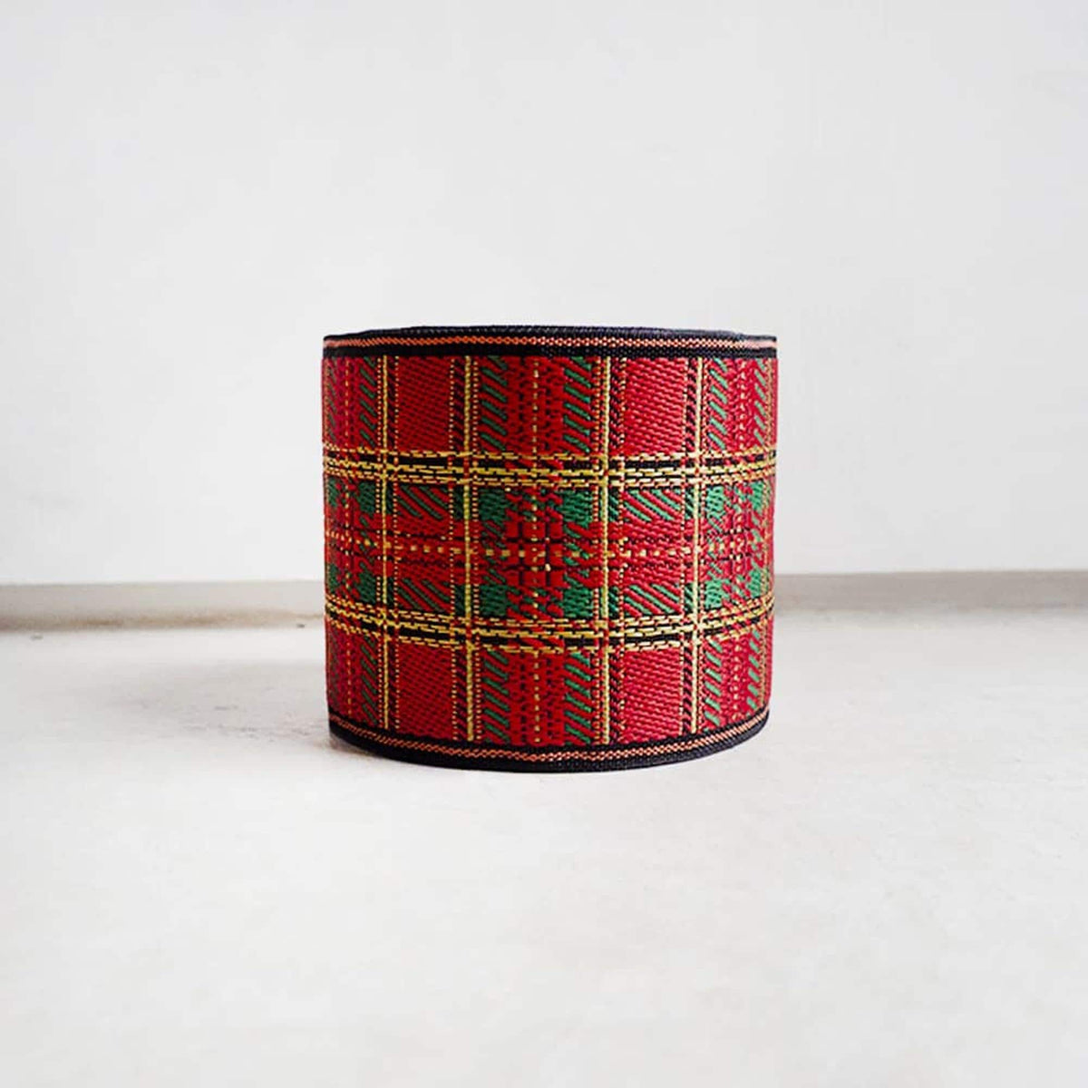A red and green plaid-patterned object, possibly a piece of fabric or a decorative item, is standing upright on a white surface against a plain background.