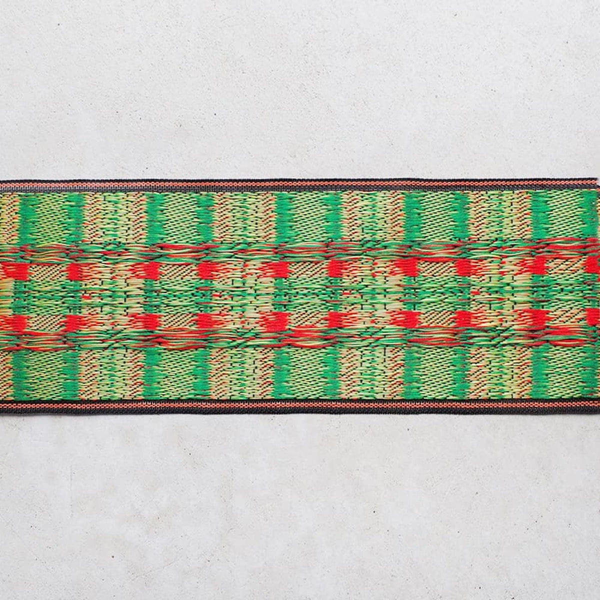 a colorful woven textile with a repeating pattern of green, red, and yellow stripes or lines.