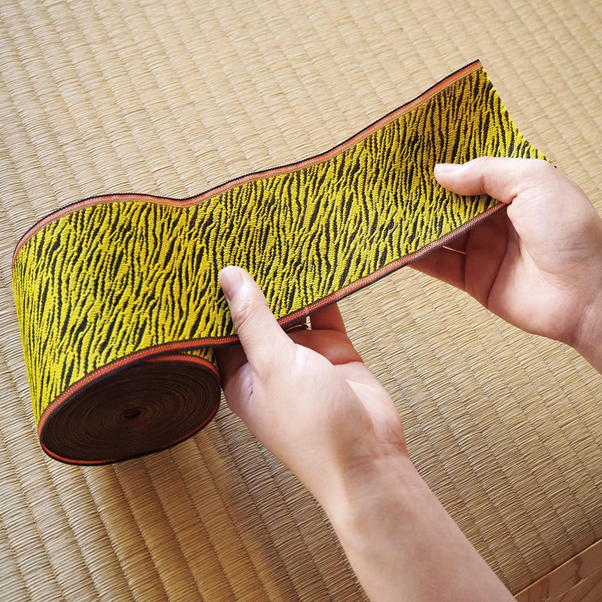 A pair of hands holding a roll of fabric with a tiger stripe pattern.
