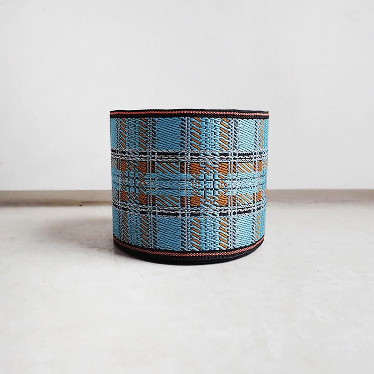 A blue and orange plaid-patterned object, possibly a container or decorative piece, is sitting on a white surface against a plain background.
