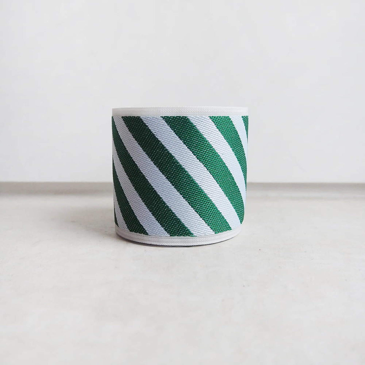 A cylindrical object with a striped pattern in green and white colors, placed on a plain white surface.