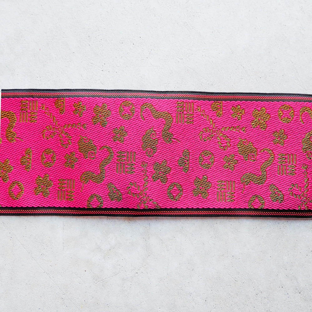 a pink fabric with a gold pattern, including various shapes and symbols, such as flowers, leaves, and geometric designs.