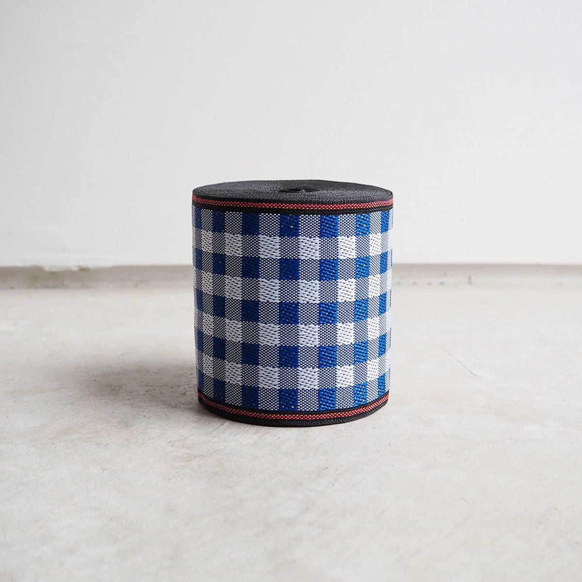 A cylindrical object with a checkered pattern in blue and white colors, sitting on a white surface against a plain background.