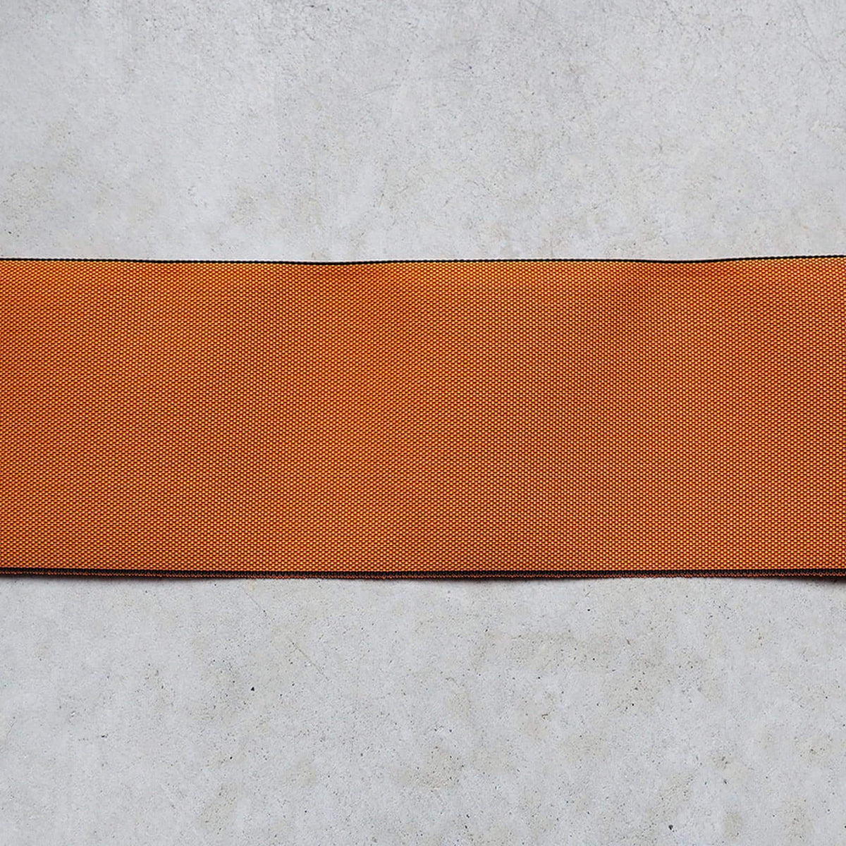 a single, horizontal orange fabric or ribbon placed on a plain, gray surface.