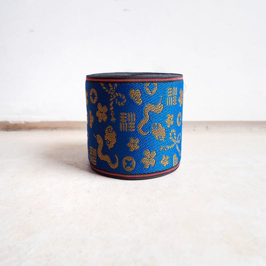 A blue and gold patterned object, possibly a piece of fabric or a decorative item, is sitting on a white surface against a plain white background.