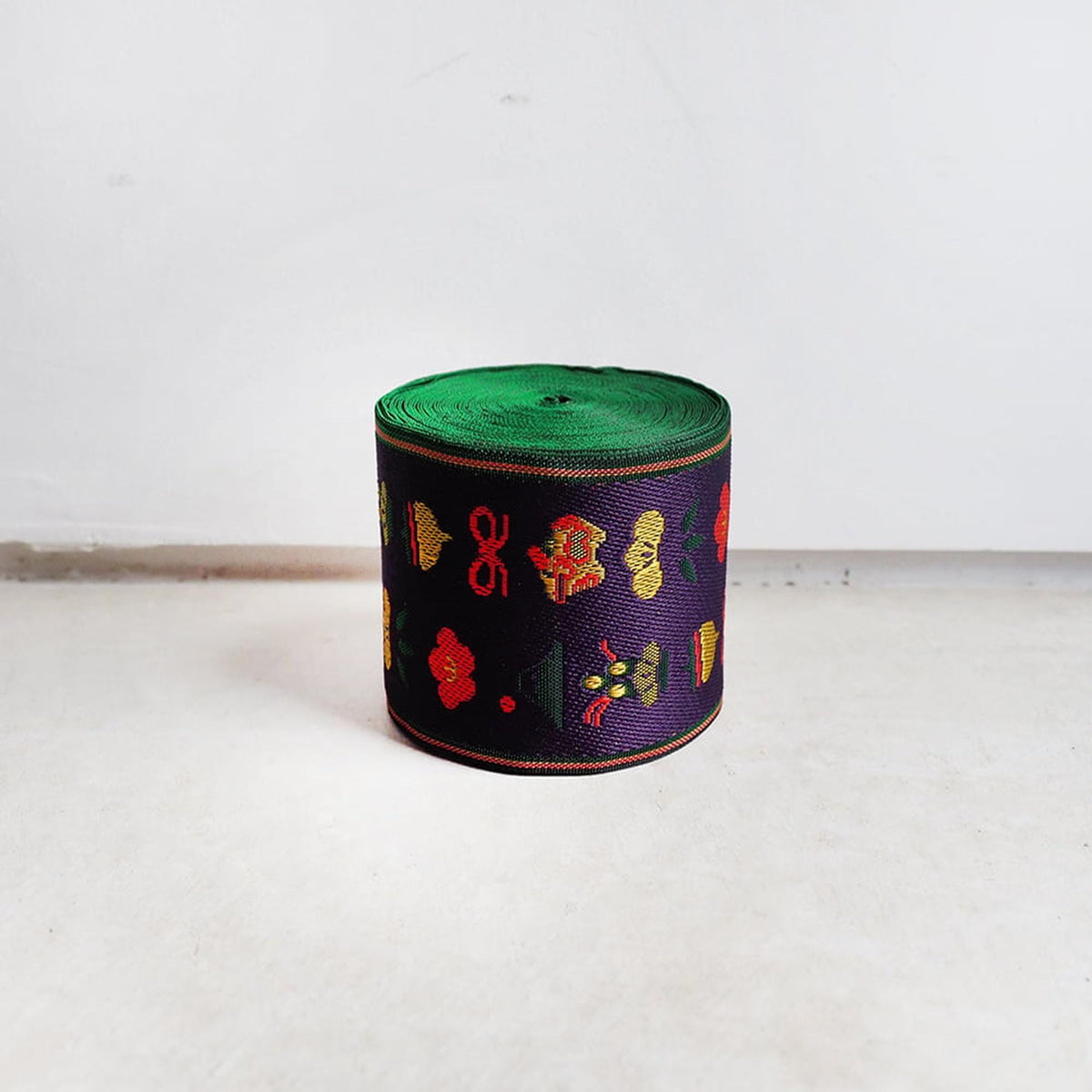 A colorful, circular object with a green top and various patterns and designs on the surface, sitting on a white floor against a plain white wall.