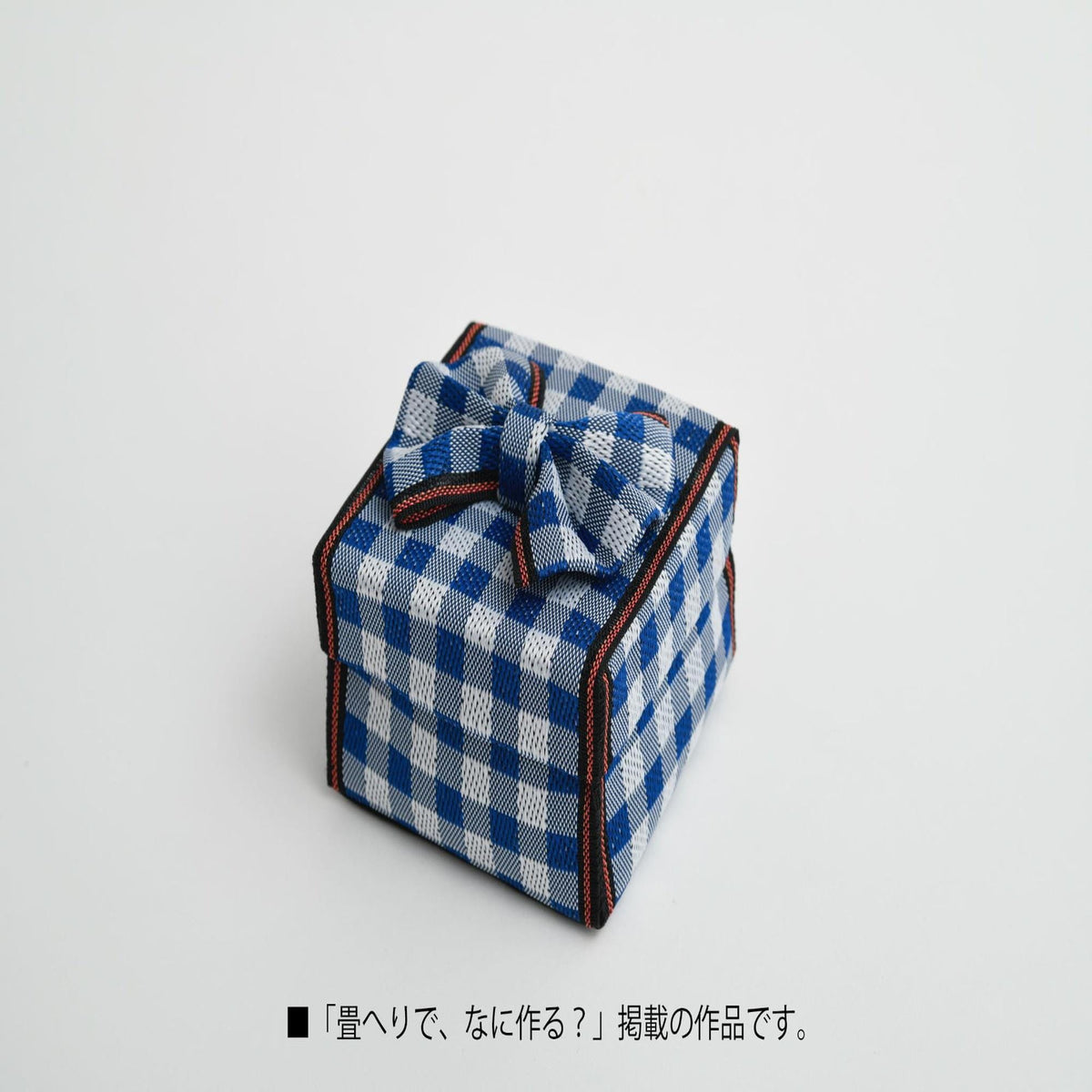 A small, square gift box with a blue and white checkered pattern and a bow, sitting on a plain white background.