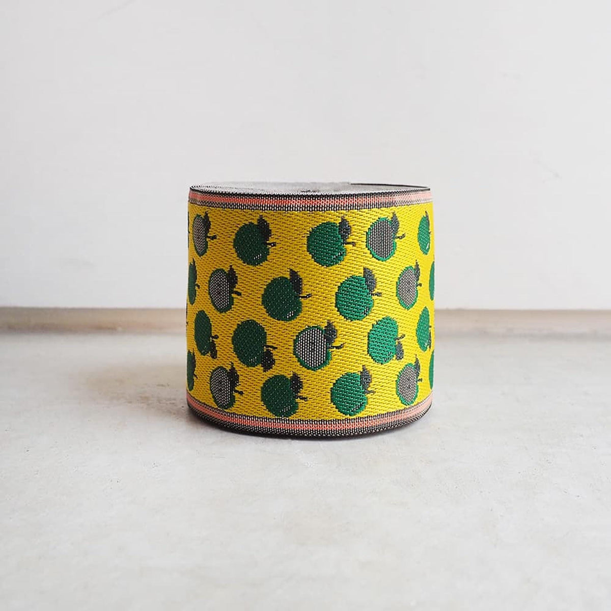 A yellow and green woven bracelet with a repeating pattern of green and yellow circles on a white background.