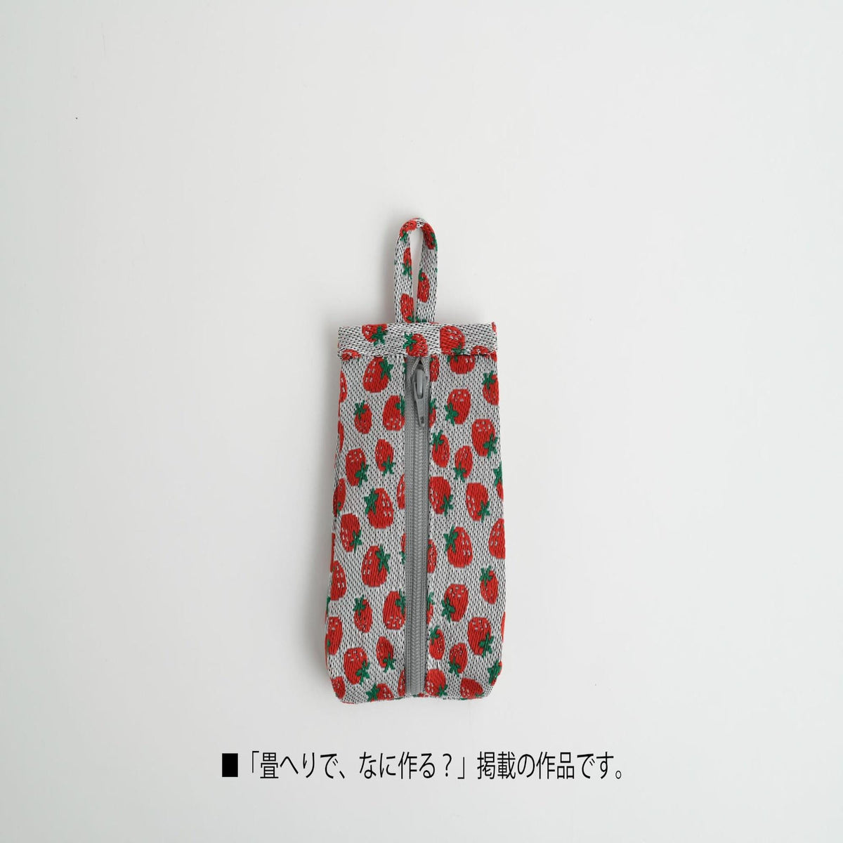 A small, square-shaped object with a red and green strawberry pattern, featuring a zipper closure.
