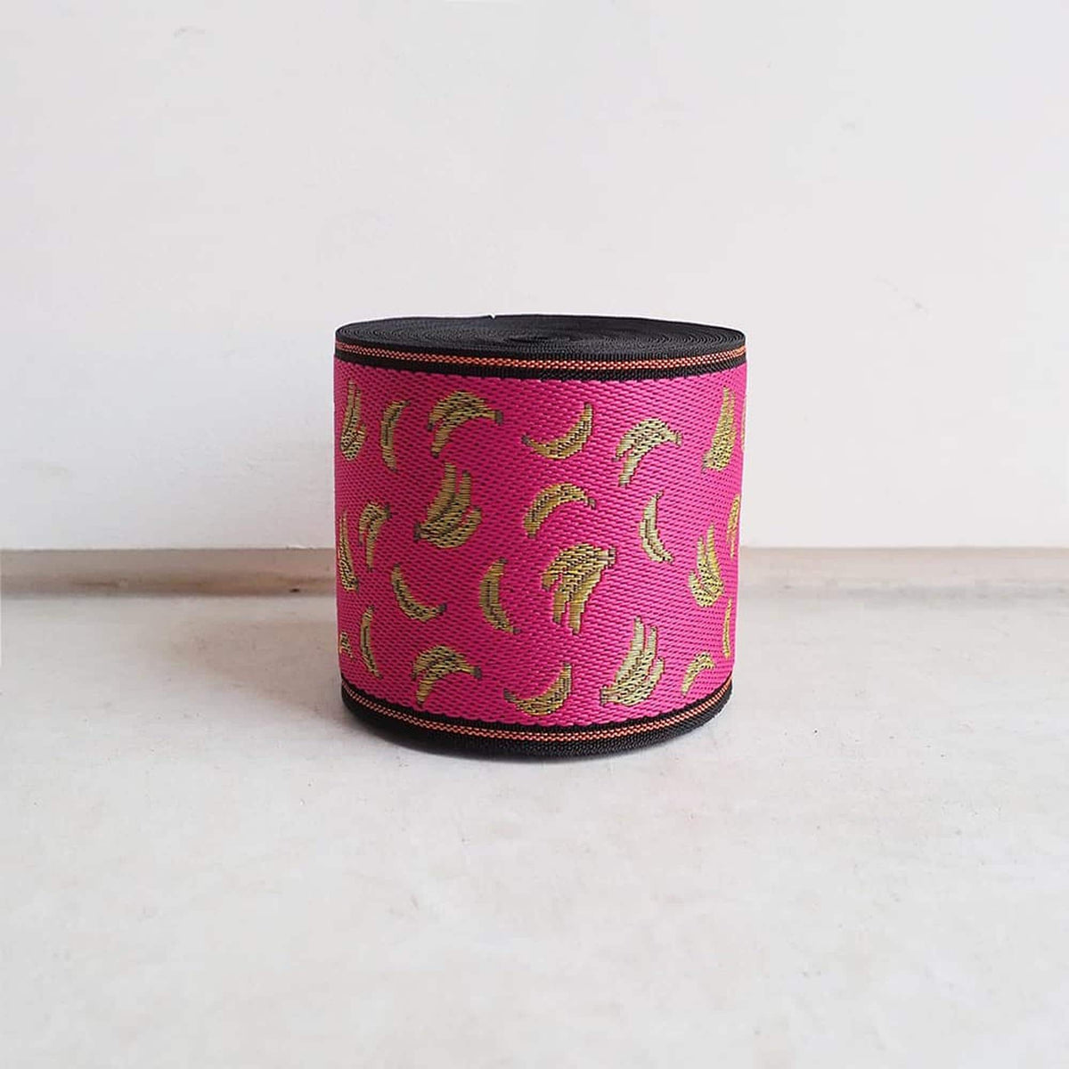 A pink and black striped object with a repeating pattern of bananas on it, sitting on a white surface against a plain background.