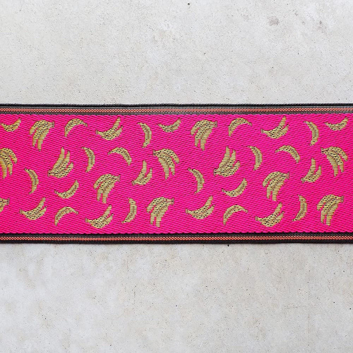 a pink fabric with a repeating pattern of gold bananas.