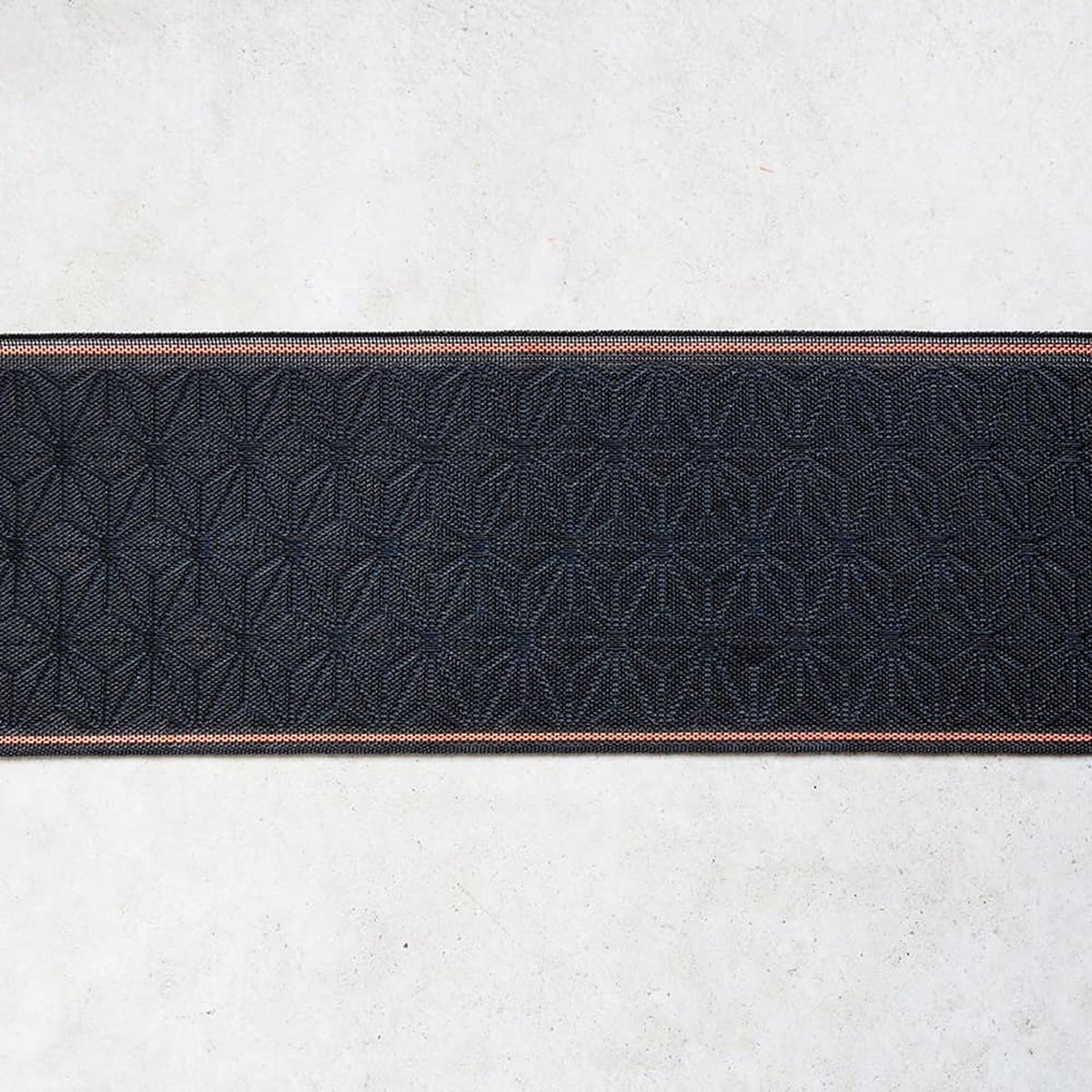 a close-up view of a black fabric with a repeating pattern of geometric shapes, such as circles and triangles, arranged in a diagonal line across the fabric.