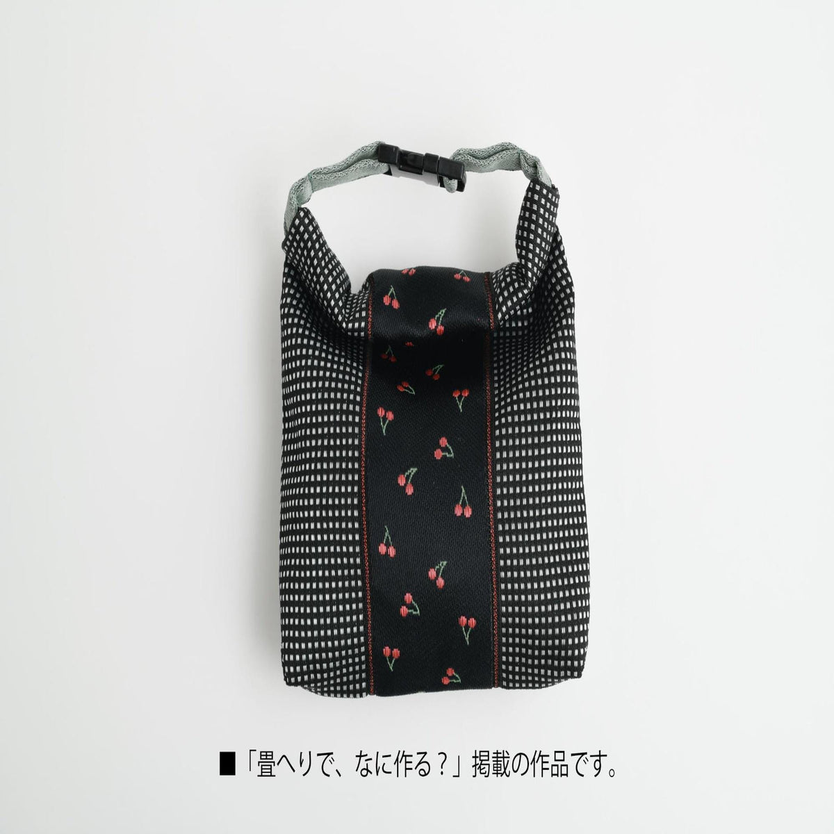 A black and white checkered bag with a pattern of red cherries on it, placed against a white background.