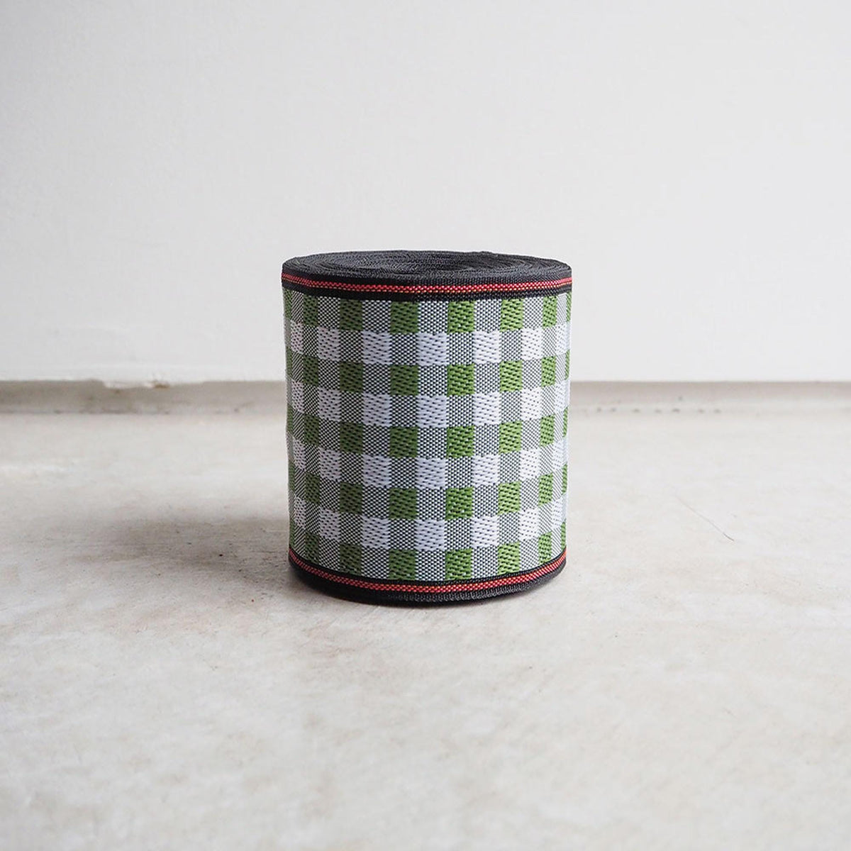 A cylindrical object with a checkered pattern in green and white colors, sitting on a white surface against a plain background.