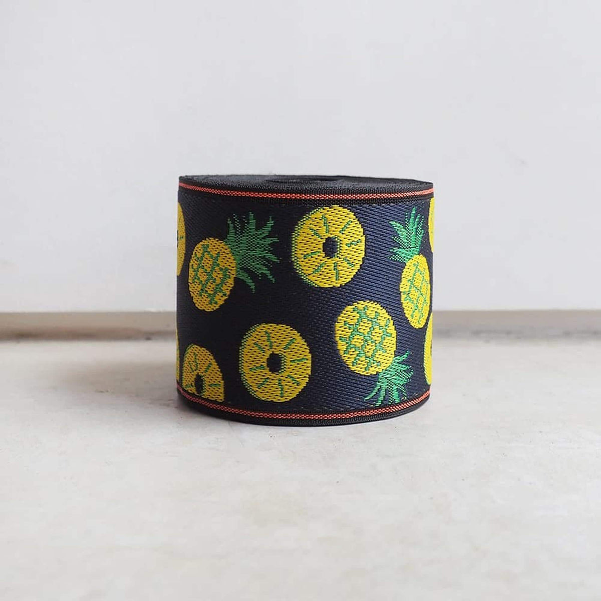 A black and yellow patterned fabric with pineapple designs on it, sitting on a white surface.