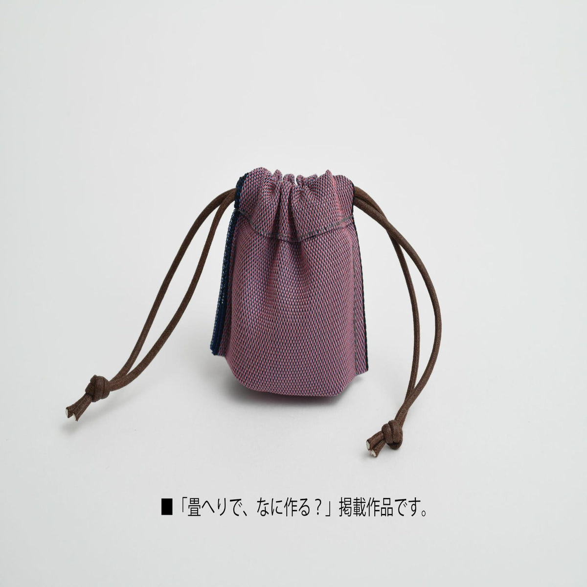 A small purple and pink woven bag with brown straps, sitting on a white background.