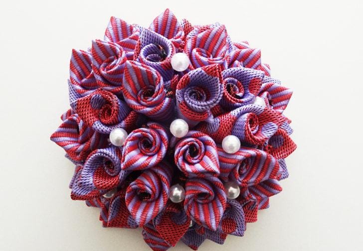 A decorative flower-shaped object made of colorful fabric, featuring red and purple stripes, and adorned with small white pearls.
