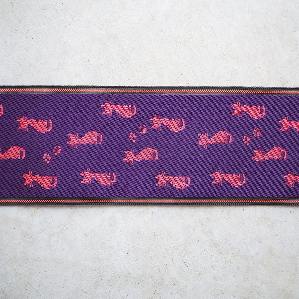 a purple fabric with a repeating pattern of pink cats on it.