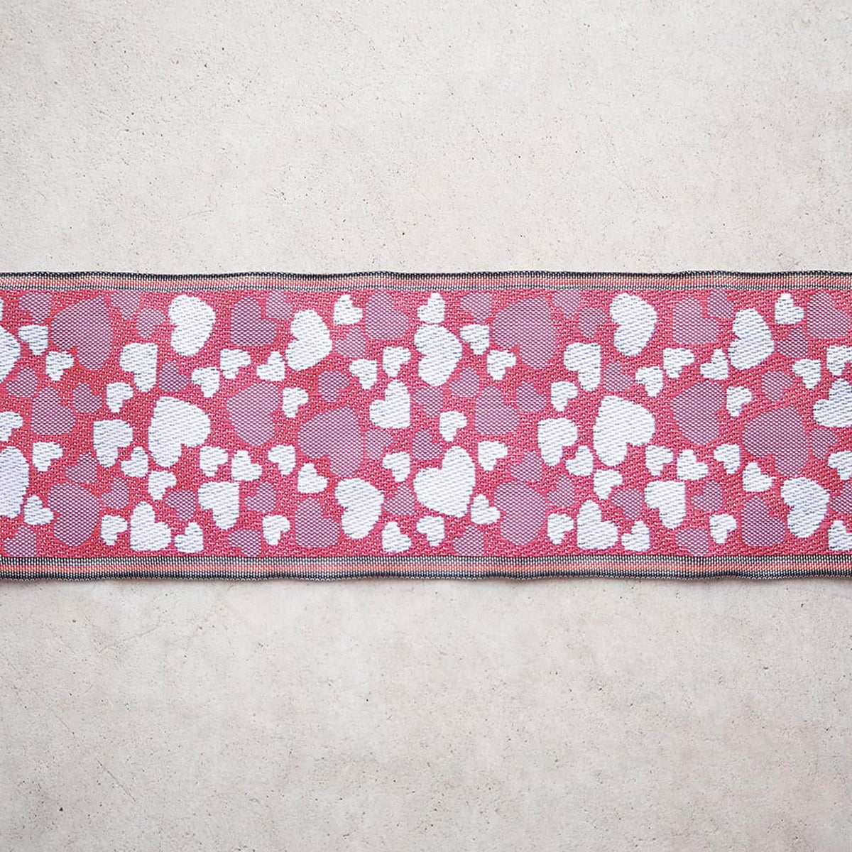 a red and white heart-patterned ribbon with a black border, placed on a plain white surface.