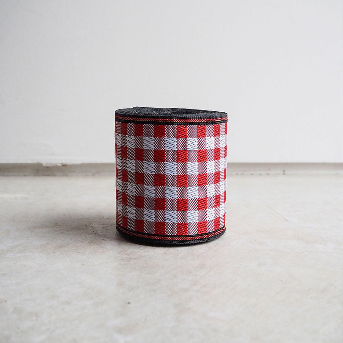 A cylindrical object with a red and white checkered pattern on a white surface.