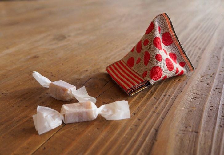 A red and white polka dot hat is placed on a wooden surface, with several wrapped candy pieces scattered around it.