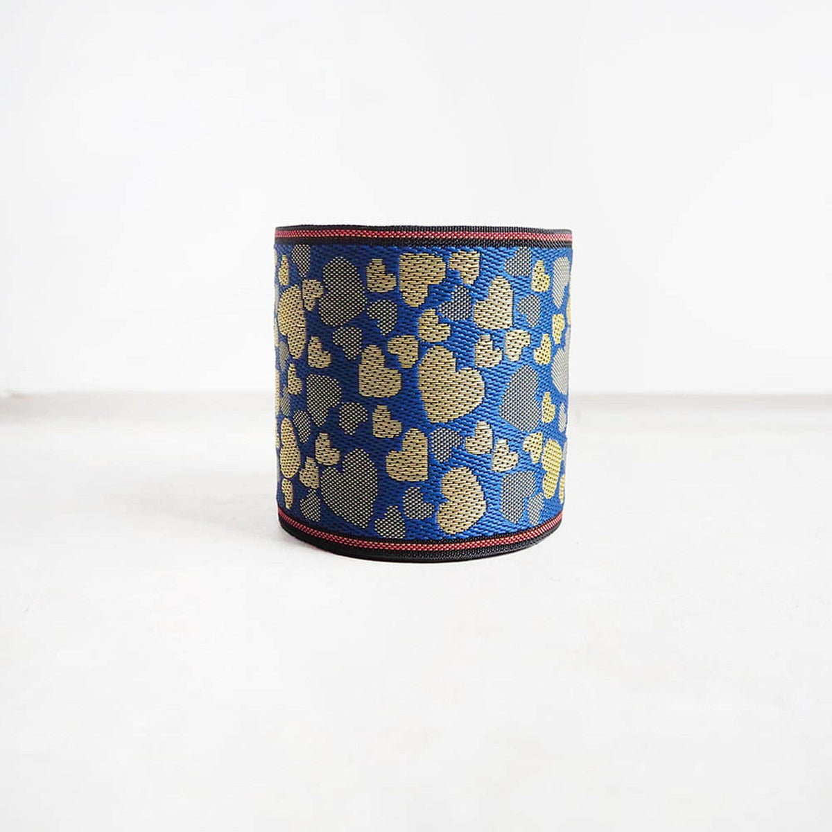 A blue and gold heart-patterned object, possibly a piece of jewelry or a decorative item, is placed on a white surface.