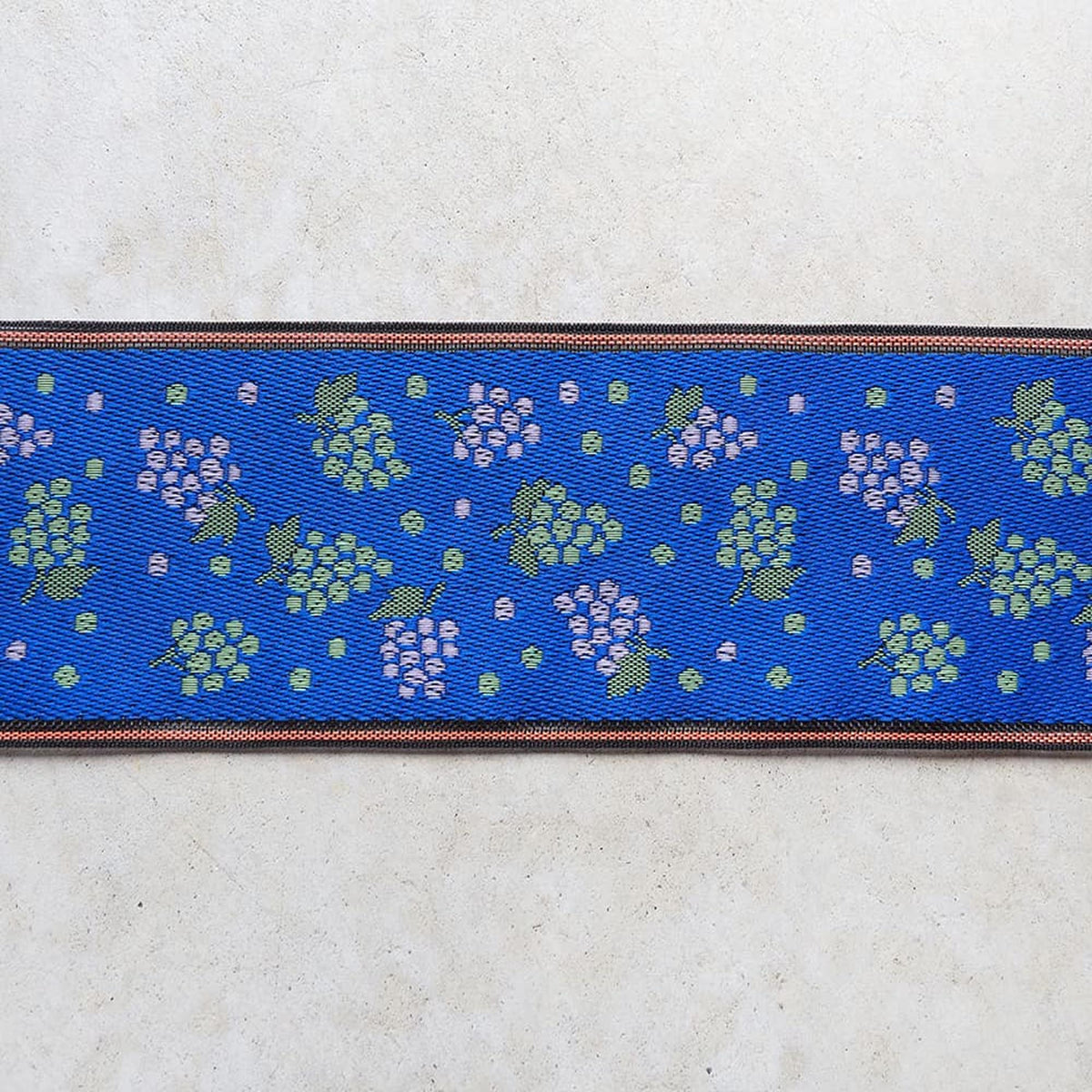 a blue fabric with a repeating pattern of green and purple grapes on a white background.
